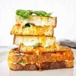 Grilled cheese sandwich cut in halves and stacked on white plate.