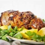 Roasted leg of lamb with lemon and parsley on white plate.