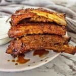 Greek Ribs on white plate with bowl of yogurt sauce in background.