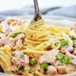 Fork being twirled in grey bowl of ham pasta.