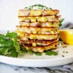 Stack of ham and corn fritters on white plate with parsley and lemon.