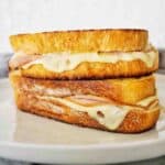 Two ham and cheese sandwiches stacked on white plate.