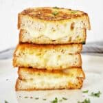 Grilled cheese sandwich stack on white plate with chopped parsley.