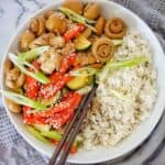 Chicken with rice and vegetables in white bowl with pair of chopsticks on top.