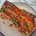 Honey Soy Pork Ribs on white plate with drips of sauce and chopped parsley