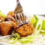 Fork pushed into pork meatball with rice and sliced green onions in the bowl.