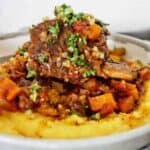 Italian short ribs in grey bowl with polenta, vegetables and sauce.