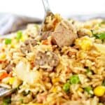 Spoon in fried rice with lamb on white plate.