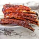 Lamb ribs stacked into a pile on white plate with grey tea towel behind.