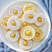 Lemon curd shortbread cookies dusted with icing sugar on white plate.