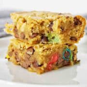 Two sliced blondies with m and m's and chocolate stacked on a white plate,