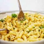 Fork being pushed into grey and white bowl of macaroni alfredo.
