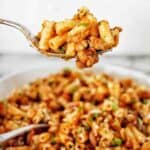 Spoon holding macaroni bolognese above white bowl of the same