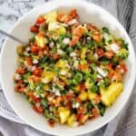 Mango and tomato salsa in a large white bowl with silver spoon.