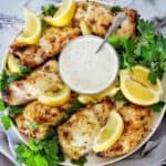 Chicken thighs on white plate with lemon wedges, parsley and bowl of sauce.