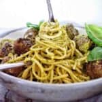 Fork being twirled in grey bowl of meatball pesto pasta.