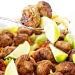Spoon holding meatballs and lime wedges above tray of the same.