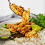 Fork holding cooked prawns above white bowl with rice and limes.