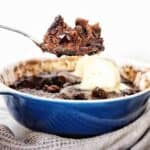 Spoon holding chocolate pudding over blue and white dish of the same.
