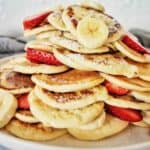 Mini Pancakes in a stack with strawberries, banana and maple syrup
