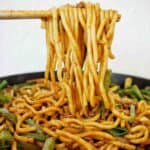 Chopsticks holding Mongolian noodles above black pan of the same.