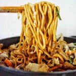Chopsticks holding noodles over a black pan of the same