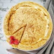 Caramel cheesecake dusted with cocoa powder and raspberries on a white plate.