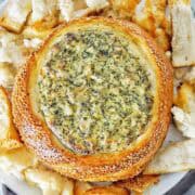 Spinach and artichoke dip in a bread bowl on white plate.