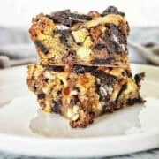 Two oreo blondies stacked on a white plate with grey napkin behind.