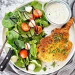 Pork chop on white plate with salad, sauce and knife and fork.