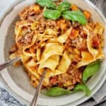 Pasta bolognese in grey bowl with fork, spoon and basil leaves.