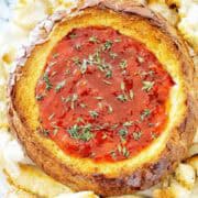 Baked pepper jelly cheese dip in bread bowl with thyme leaves on top.