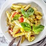 Pesto paste bake in white bowl with fork, spoon and basil leaves.
