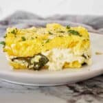 Slice of spinach polenta bake on white plate with grey napkin behind.