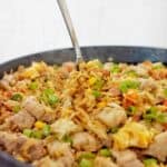 Spoon in large black pan of fried rice.