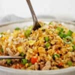 Fork in grey bowl of pork fried rice.