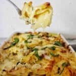 Spoon holding potato bake above white baking dish of the same.