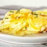 Potato bake with onions and cheese topping on white plate.
