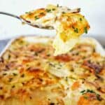 Spoon holding potato bake over white baking dish of the same.
