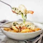 Fork holding risotto above grey and white bowl of the same.