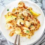 Pasta with prawns on white plate with fork and spoon.