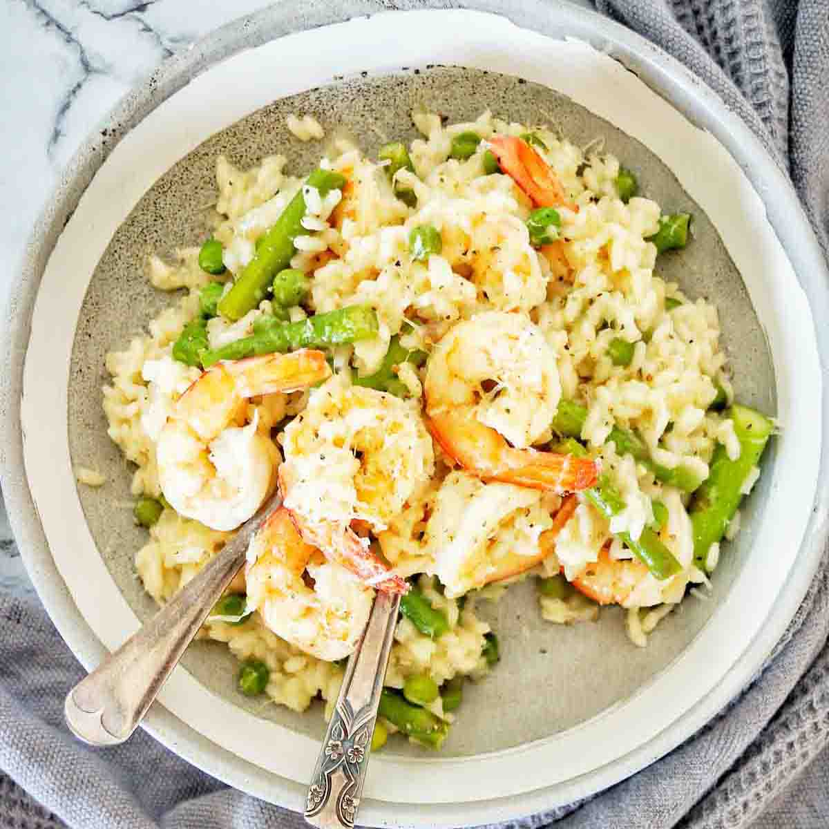 Risotto with prawns and asparagus in grey bowl with fork and spoon.