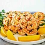 Prawn skewers with lemon and parsley on white plate.