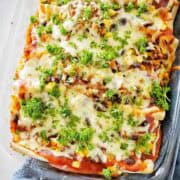 Pulled pork enchiladas topped with cheese and garnish with parsley in baking dish.