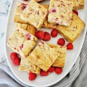 Raspberry white chocolate blondies on white serving platter with extra raspberries.