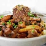 Red wine short ribs in grey bowl with vegetables and parsley.