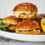 Roast beef sliders on white plate with parsley and lemon wedges.