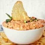 Chip sticking up in bowl of dip with chips around the base of it.