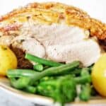 Oven baked pork roast on white plate with greens and potatoes.