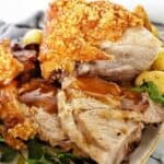 Sliced roast pork with crackling and gravy on white plate.